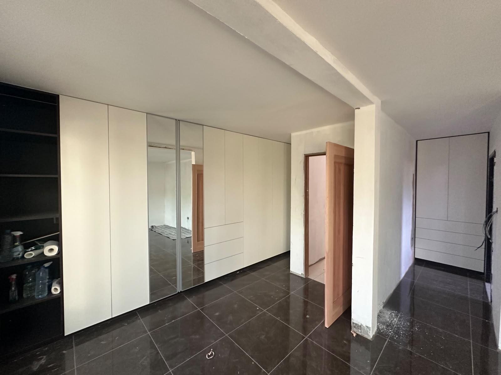 Built-in white wardrobes with a mirrored door and a polished dark tile floor